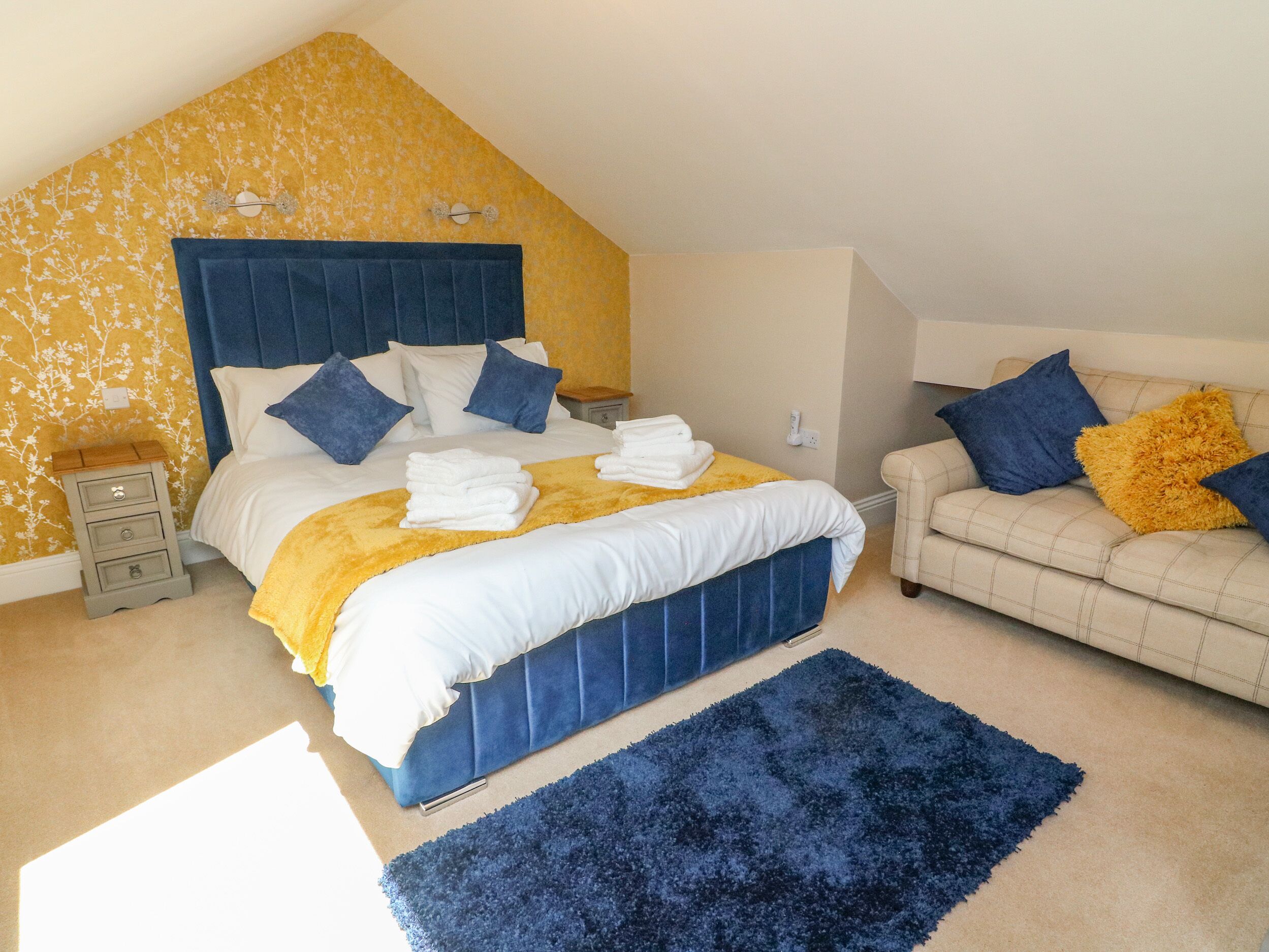 Une chambre à coucher avec un lit, une table de chevet, un canapé et un tapis bleu.