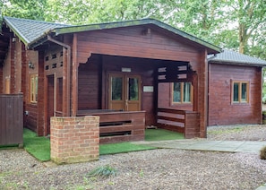 A rustic wooden building with a porch, a brick foundation, and a small grassy area in front. - Spacious and comfortable lodge with contemporary styling. (Ellesmere)