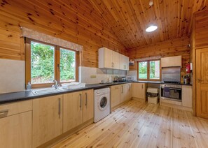 Eine Holzhütte mit Küche, einer Waschmaschine, einem Backofen und großen Fenstern.