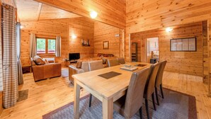 A wooden cabin interior with a dining table, chairs, a sofa, a TV, and a window. - Spacious and comfortable lodge with contemporary styling. (Ellesmere)