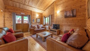 A log cabin interior with a wooden ceiling, leather sofas, a coffee table, a television, and a painting on the wall. - Spacious and comfortable lodge with contemporary styling. (Ellesmere)