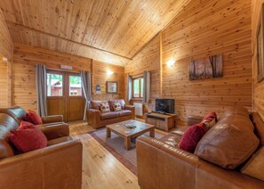 A log cabin interior with a wooden ceiling, leather sofas, a coffee table, a television, and a painting on the wall. - Spacious and comfortable lodge with contemporary styling. (Ellesmere)