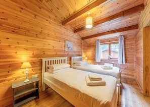 A wooden cabin room with two beds, a window, and a lamp. - Spacious and comfortable lodge with contemporary styling. (Ellesmere)
