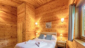 A wooden-paneled room with a bed, bedside lamps, and a window. - Spacious and comfortable lodge with contemporary styling. (Ellesmere)