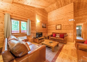 A log cabin interior with a sofa, a television, a coffee table, and a window with curtains. - Spacious and comfortable lodge with contemporary styling. (Ellesmere)