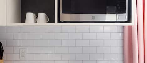 A kitchen with white cabinets, a microwave, a stove, and a shelf with a yellow bottle and glass jars.