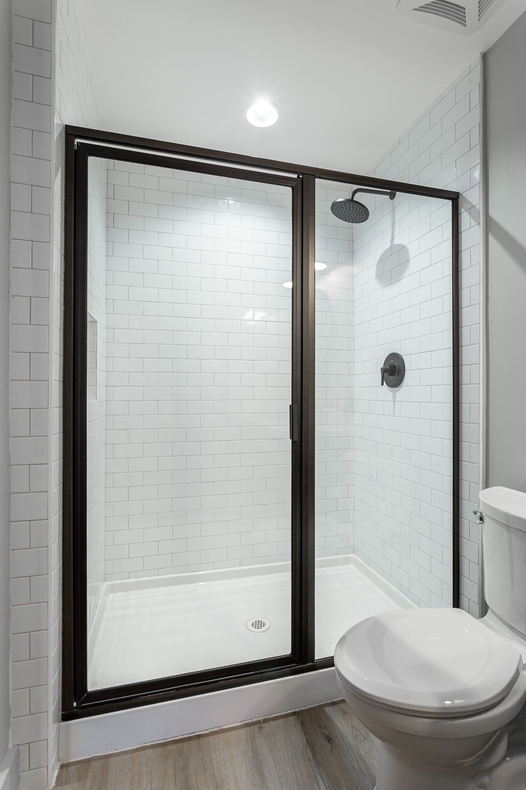 A modern bathroom with a glass-enclosed shower, white tiled walls, and a white toilet.