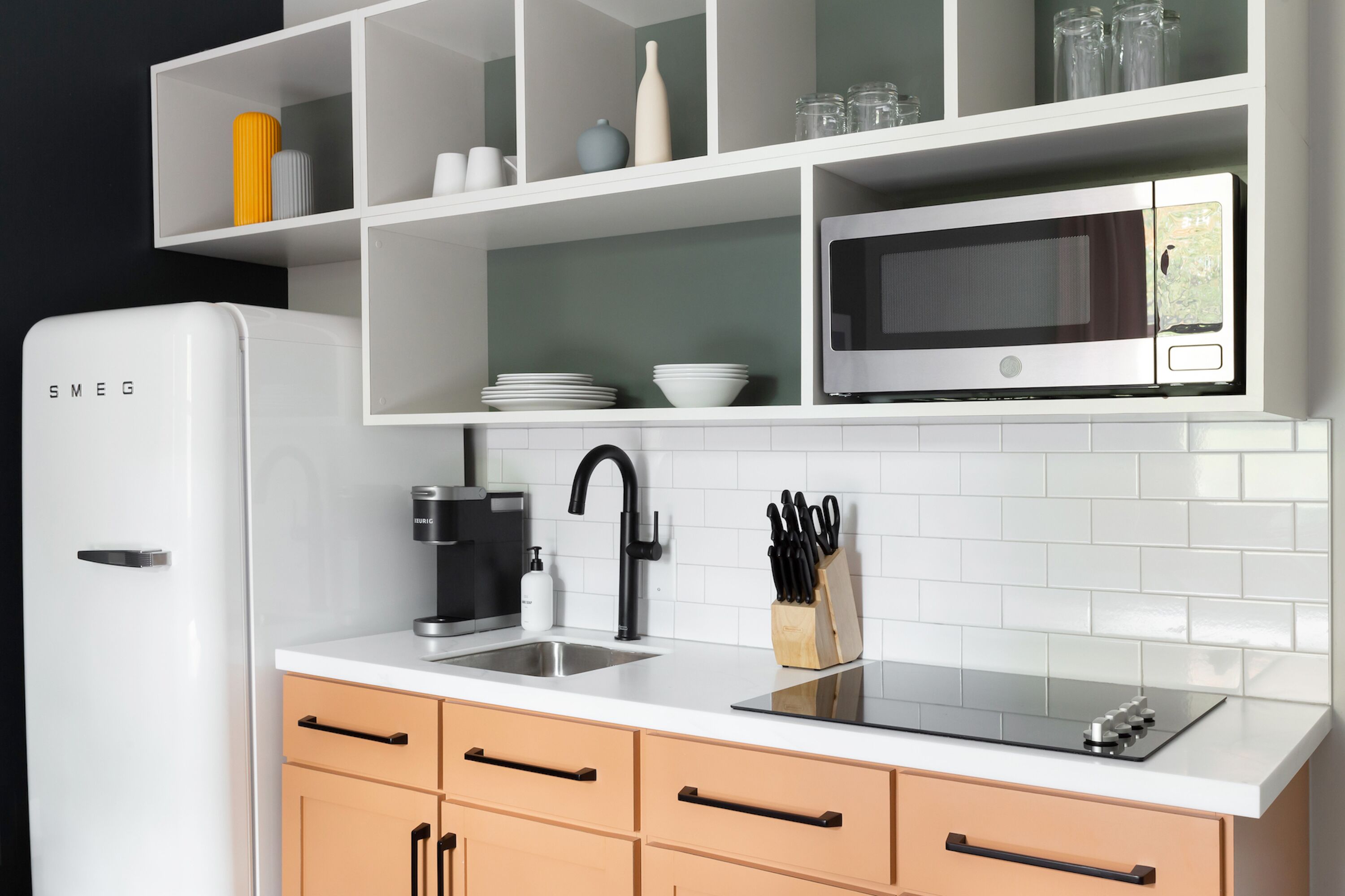 A modern kitchen with white cabinetry, a built-in microwave, a sink, and a coffee maker.