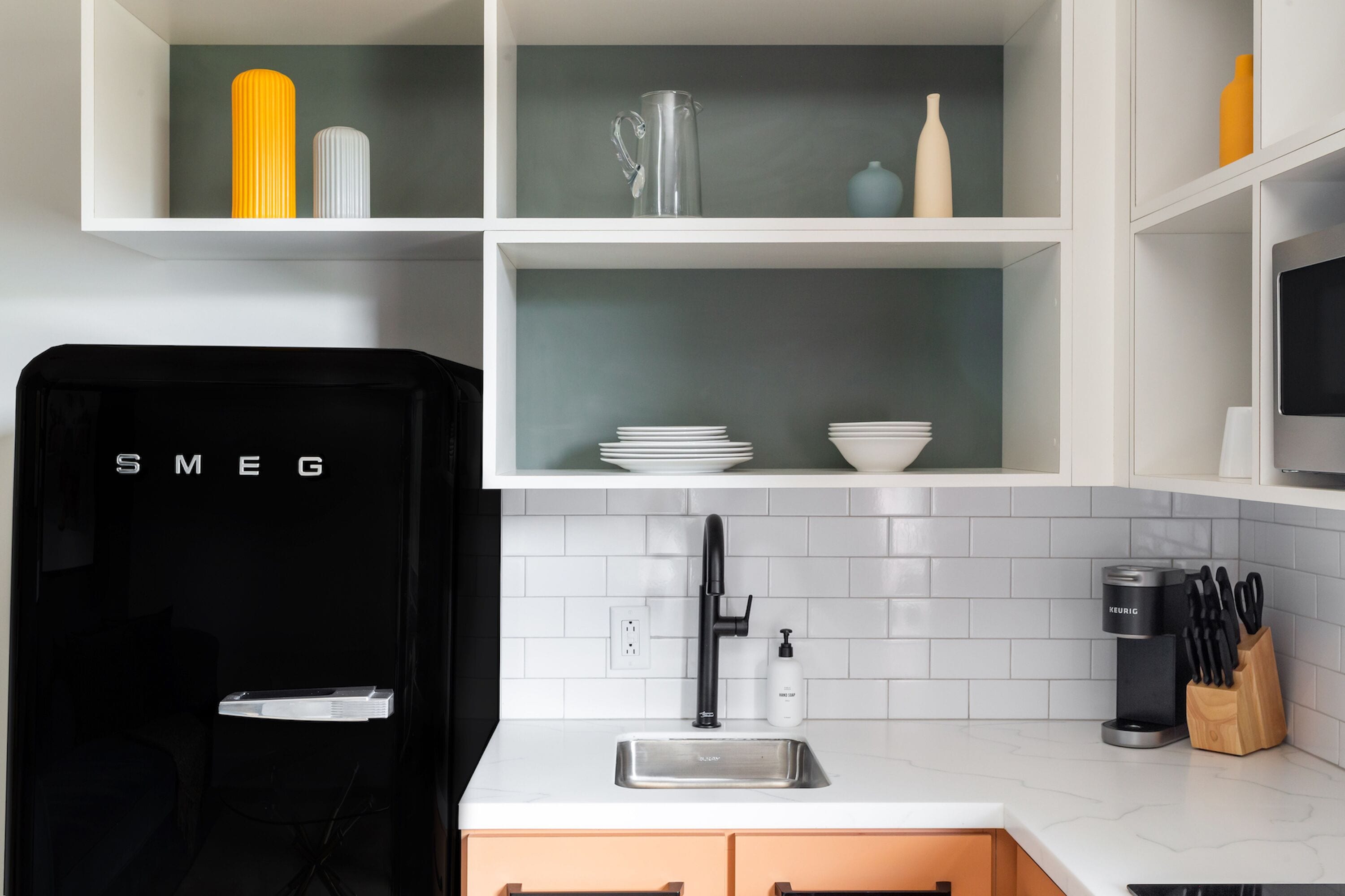 A modern kitchen with white cabinets, a black refrigerator, a stainless steel sink, and a coffee maker.