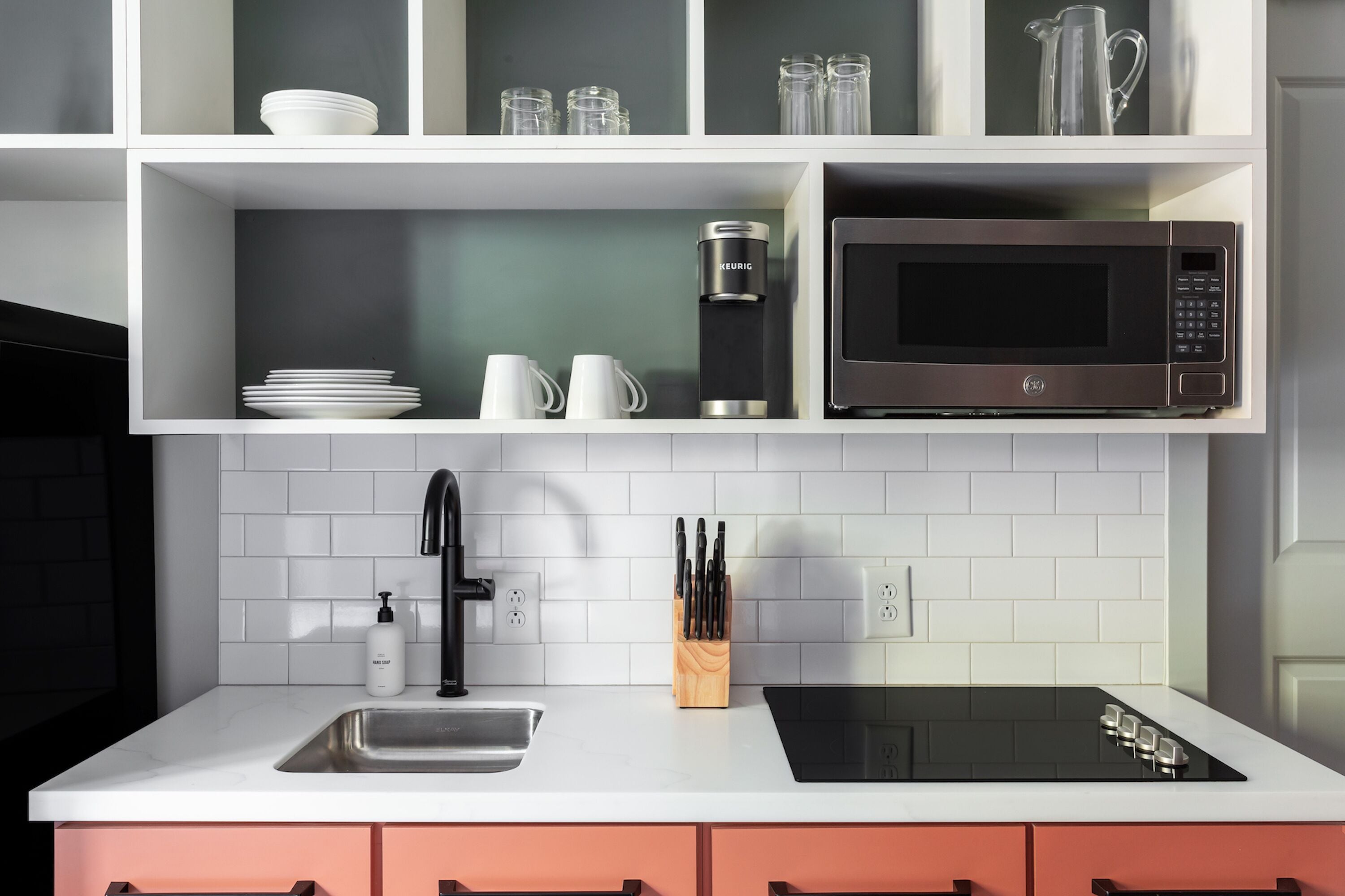 Una cocina moderna con armarios blancos, una hornalla negra, un lavamanos de acero inoxidable y un microondas.