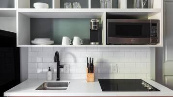 Una cocina moderna con armarios blancos, una hornalla negra, un lavamanos de acero inoxidable y un microondas.