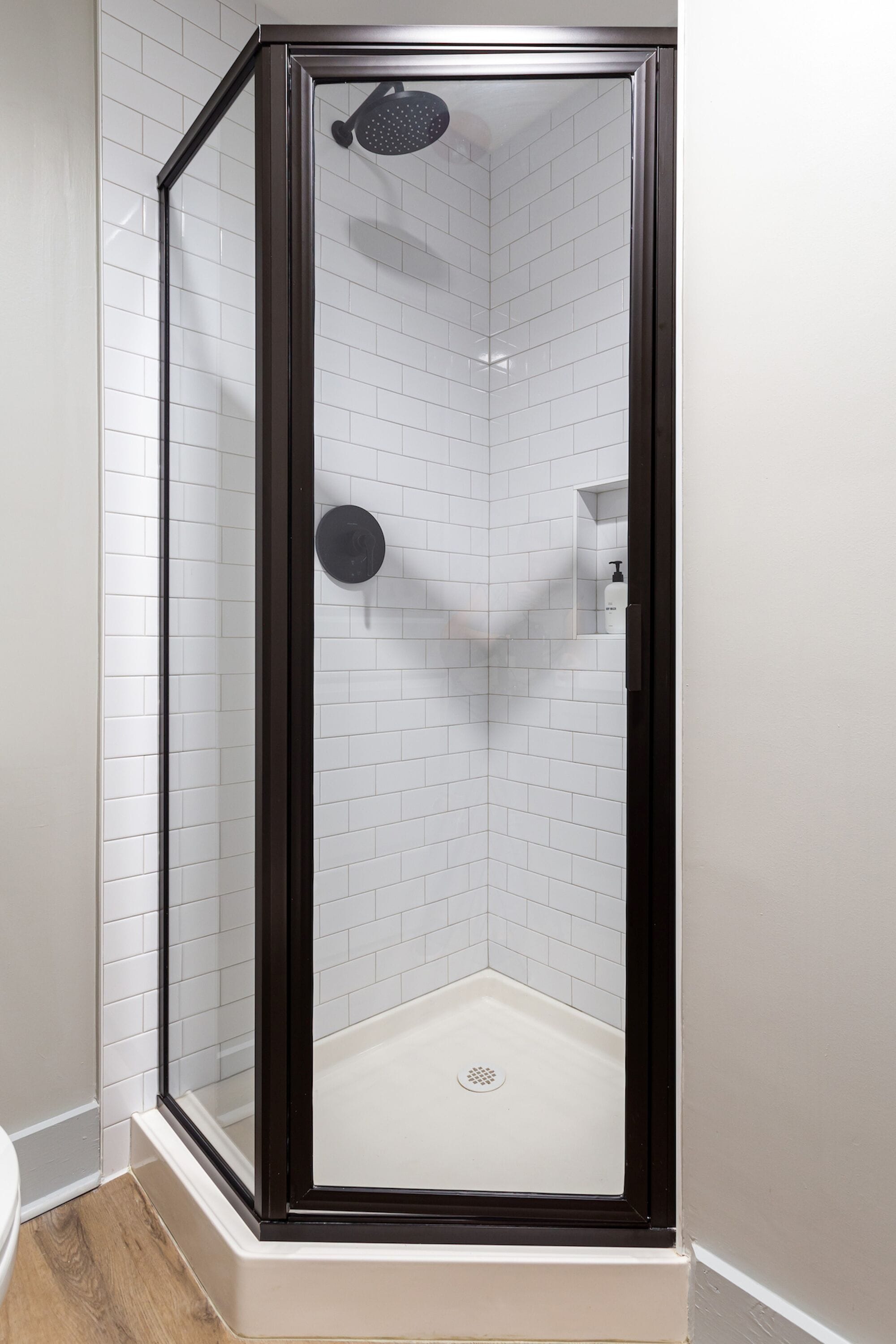 A glass-enclosed shower with white tiled walls and a black frame.