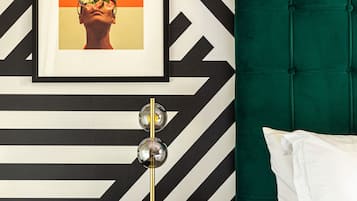 A modern bedroom with a black and white chevron-patterned wall, a green upholstered headboard, a bedside table with a gold lamp, and a framed picture above the bed.