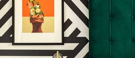 Une chambre moderne avec un mur orné d’un motif en chevrons noir et blanc, une tête de lit rembourrée de couleur verte, une table de chevet avec une lampe dorée et un tableau encadré au-dessus du lit.