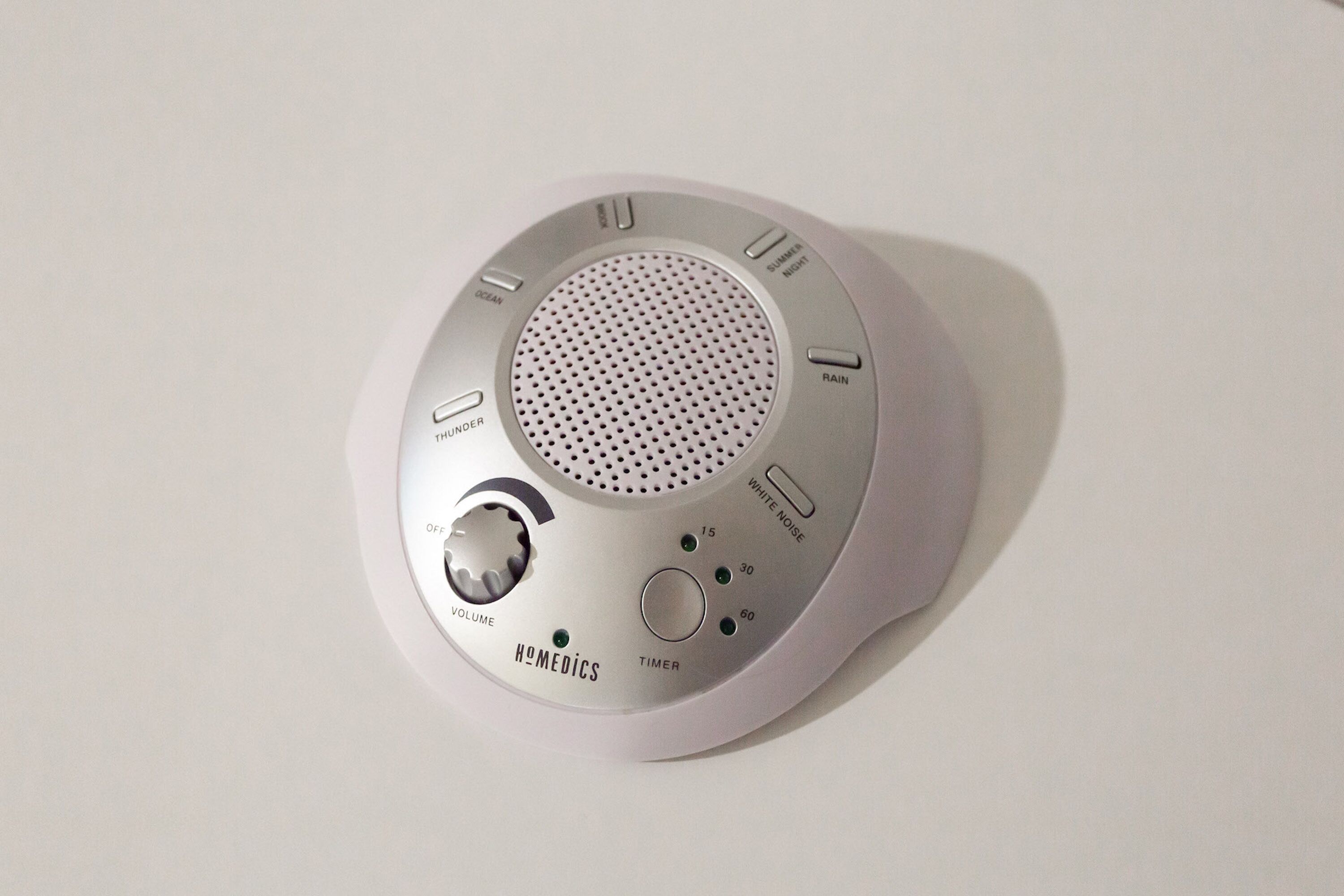 A white, circular, portable speaker with volume control, timer, and sound settings.