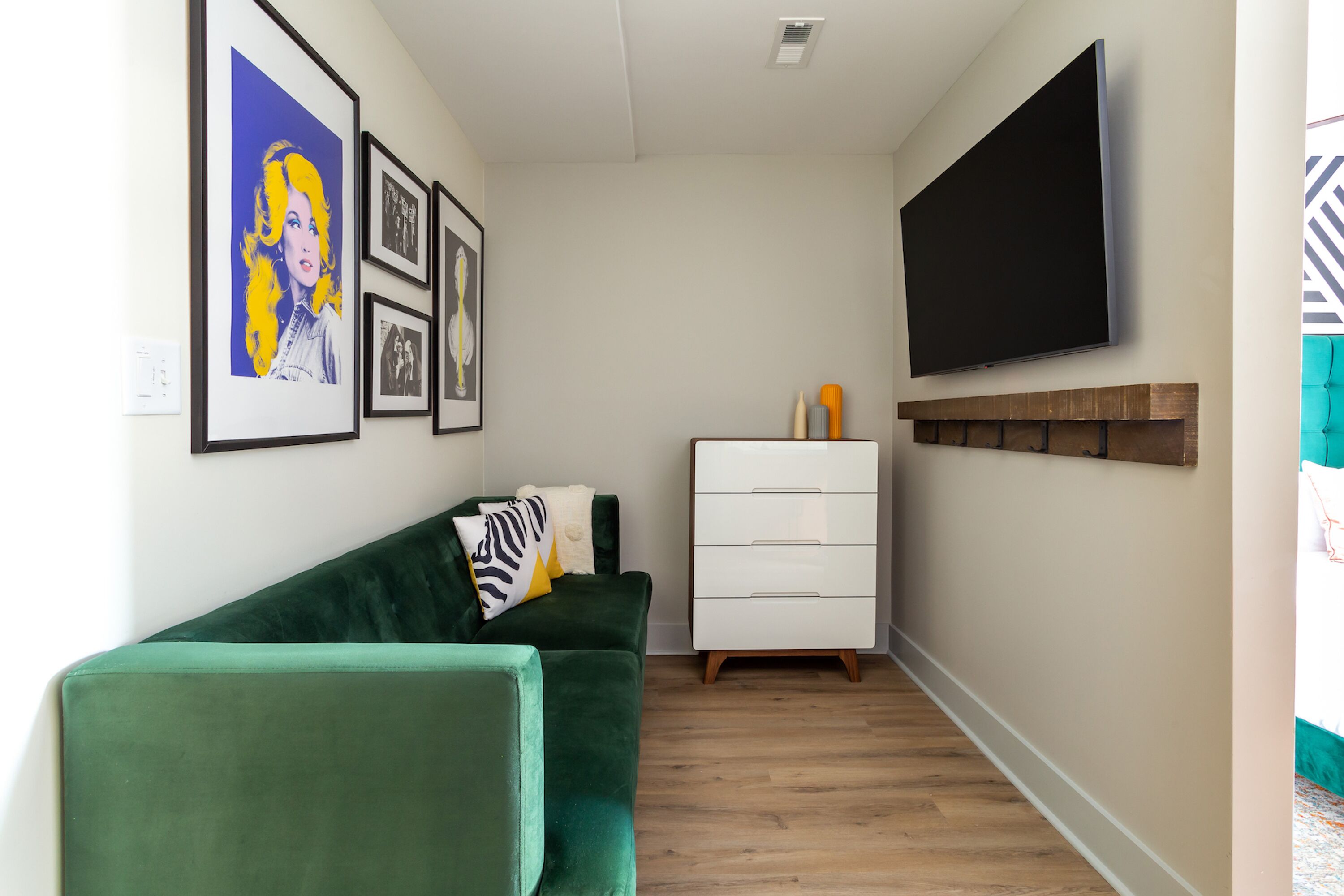 A modern living room with a green sofa, a white dresser, and a flat-screen TV mounted on the wall.