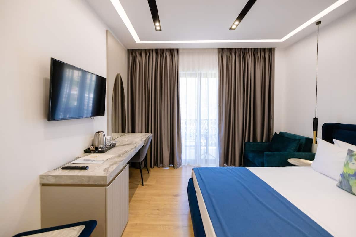 A hotel room with a bed, a desk with a TV, a chair, and a window with curtains.