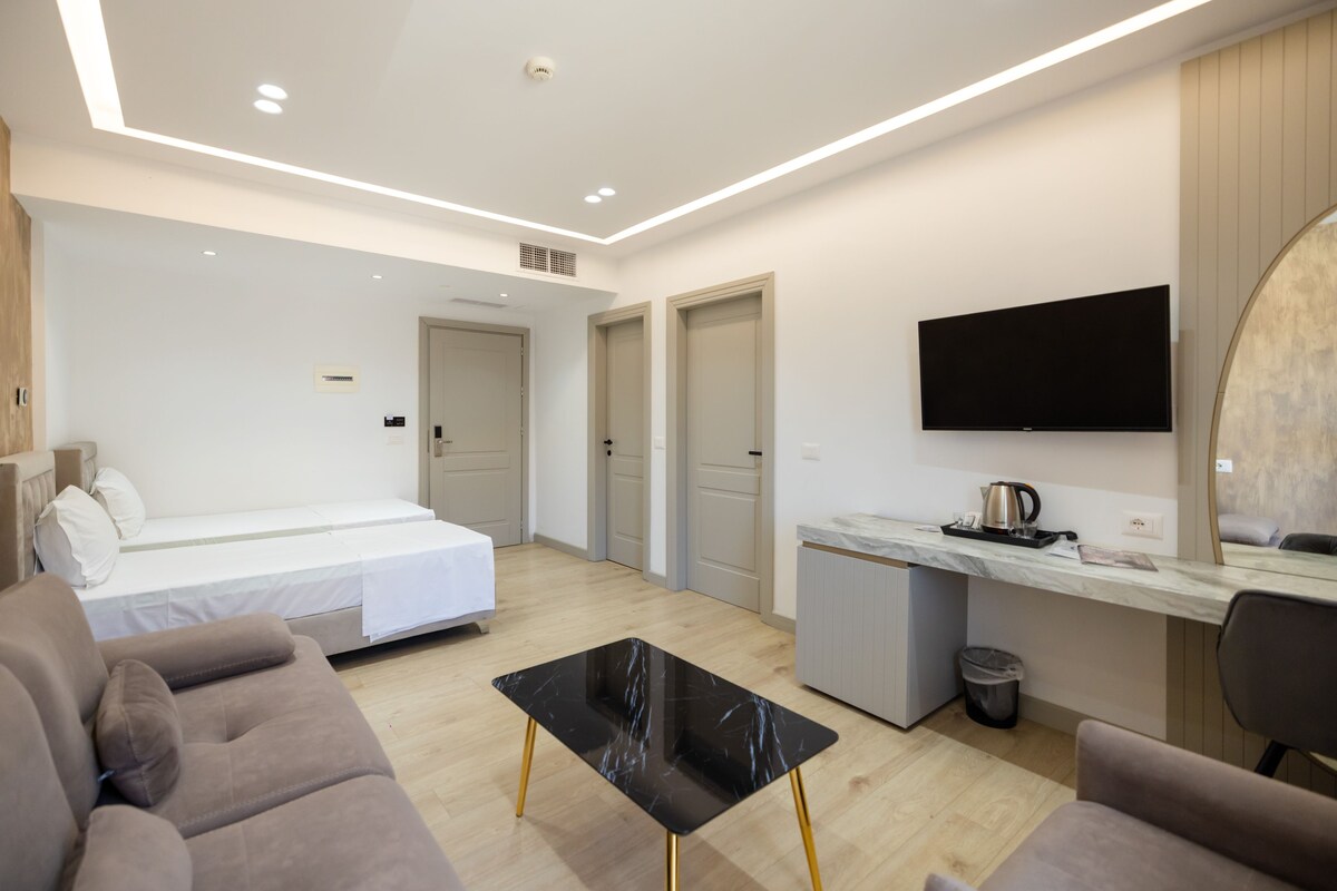 A modern hotel room with a bed, a desk, a TV, and a sofa.