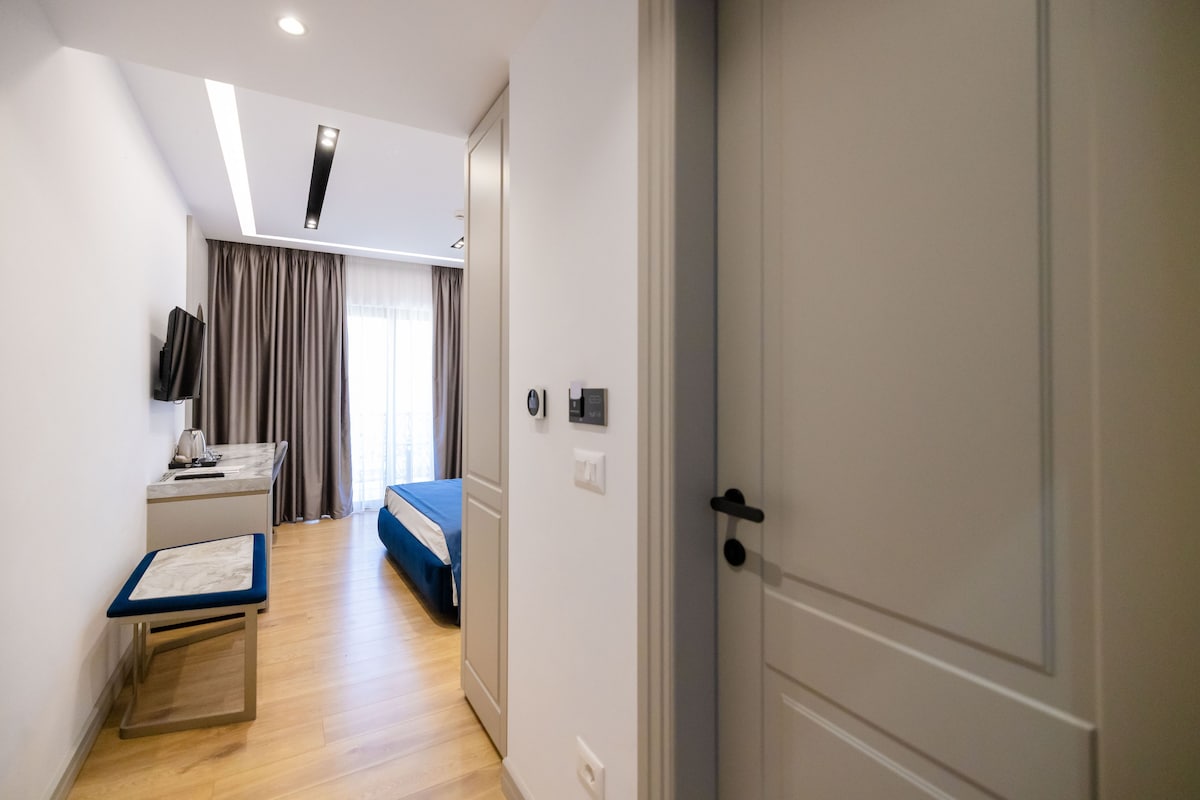 A hotel room with a bed, a desk, a chair, a TV, and a door.