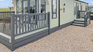 Ein Bungalow mit Veranda, einer kleinen Terrasse und einer Einfahrt mit Kies.