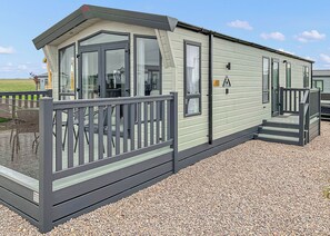 A single-story mobile home with a porch, a small deck, and a gravel driveway.