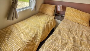 Ein Doppelbett mit gemustertem Überwurf, ein Nachttisch mit Lampe und ein Fenster mit Vorhängen.