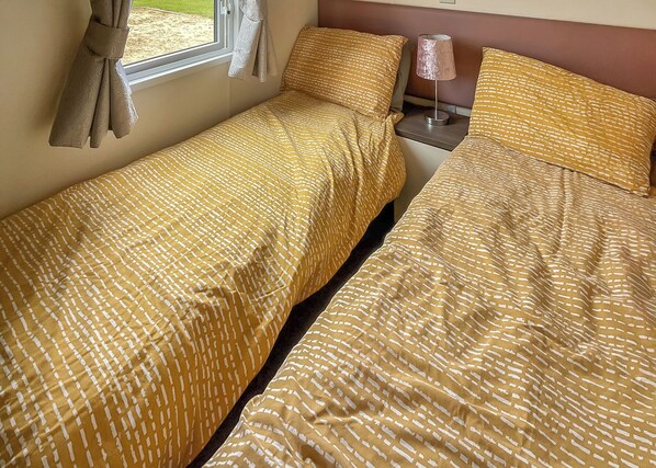A twin bed with a patterned bedspread, a bedside table with a lamp, and a window with curtains.