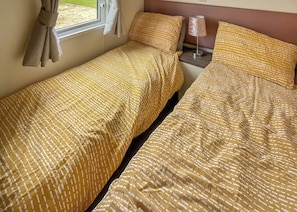 Ein Doppelbett mit gemustertem Überwurf, ein Nachttisch mit Lampe und ein Fenster mit Vorhängen.