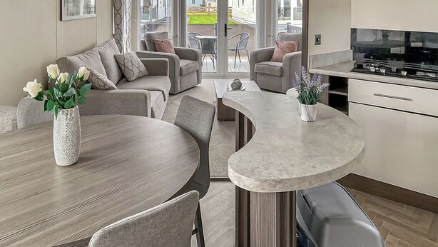 A modern kitchen with a curved island, a dining area with a round table, and a seating arrangement with sofas and chairs. - Spacious and comfortable holiday home featuring your own private hot tub. (Laurenkirk)