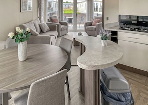 Eine moderne Küche mit einer gewölbten Kücheninsel, einem Essbereich mit rundem Tisch sowie einer Sitzecke mit Sofas und Sesseln.