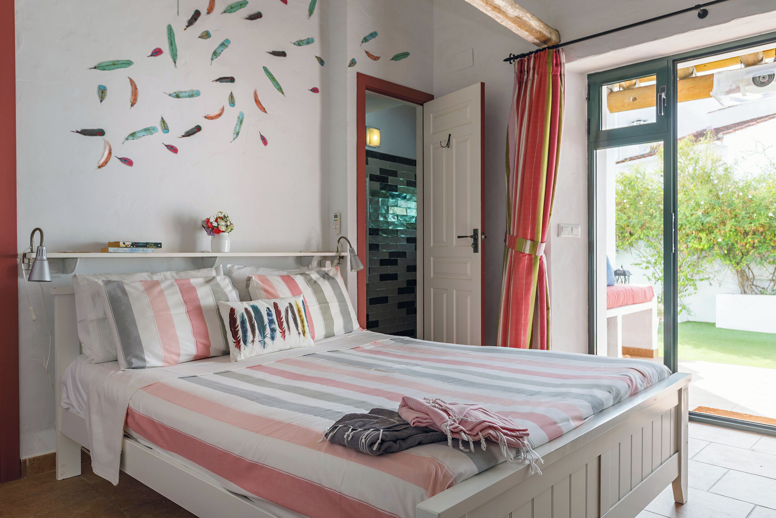 A bedroom with a bed, pillows, a bedside table, a wall decoration, and a sliding glass door to an outdoor area.