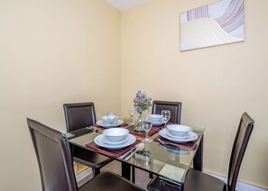 A dining table set with plates, glasses, and a vase of flowers, surrounded by chairs.
