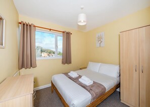 A bedroom with a bed, a wooden wardrobe, a desk, a window with curtains, and a ceiling light.