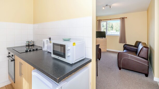 Eine kleine Küche mit Mikrowelle, Wasserkocher und Toaster, ein Essbereich mit Ledersessel und ein Fenster mit Vorhängen.