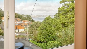 Blick aus einem Fenster auf eine Küstenlandschaft mit Gebäuden, Grünflächen und blauem Himmel.