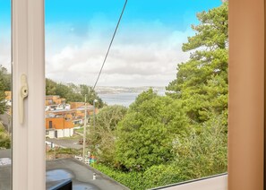 A view from a window overlooking a coastal area with buildings, greenery, and a clear sky.
