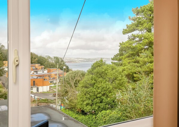 A view from a window overlooking a coastal area with buildings, greenery, and a clear sky.
