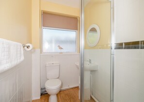 A bathroom with a toilet, a sink, a shower, and a window with a bird.