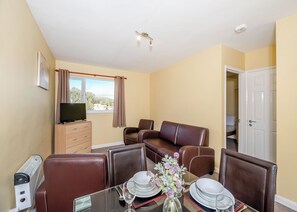 A hotel room with a dining table set for four, a sofa, a TV, and a window with curtains.