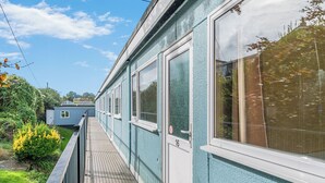 Ein Wohnhaus mit Balkon, einer mit der Nummer 16 gekennzeichneten Tür und einem Gartenbereich mit Grünflächen und einer kleinen Gartenhütte.
