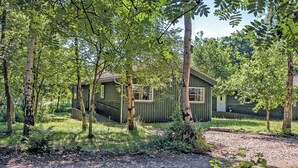 A cabin with a porch, surrounded by trees and a gravel path.