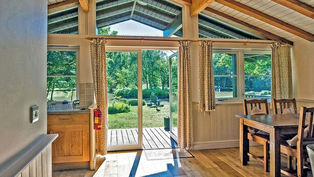 A room with a wooden table and chairs, a fire extinguisher, and a view of a garden through a glass door.