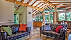 A spacious living area with two leather sofas, wooden flooring, and a high ceiling with exposed beams.