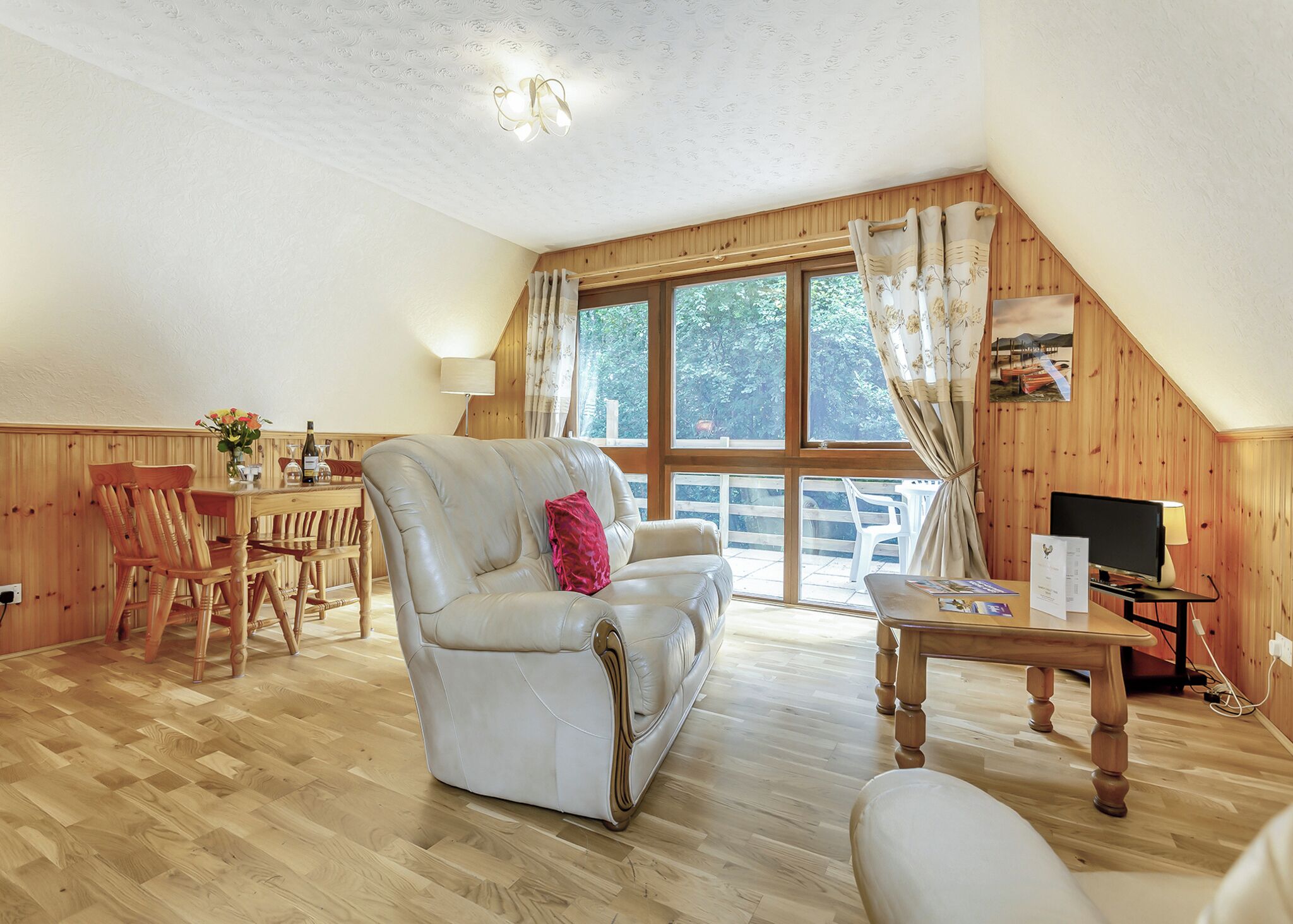 Una sala de estar acogedora con sofá, mesa de comedor y sillas, paredes de madera y ventanas amplias.