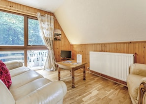 Ein gemütliches Zimmer mit Holzvertäfelung, einer Couch, einem Tisch mit Fernseher und einem Fenster mit Vorhängen.
