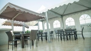 Un espace extérieur aménagé avec des tables et des chaises, protégé par un auvent et doté de grandes fenêtres.