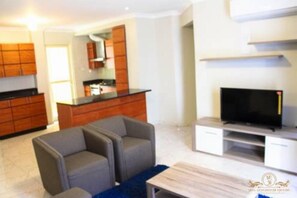 Una sala de estar moderna con un televisor de pantalla plana, sofás grises y una mesa de centro de madera.