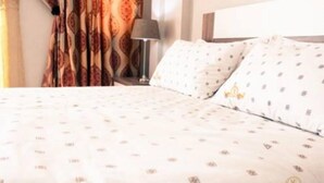 Une chambre d’hôtel avec un lit, des rideaux à motifs, une table de chevet et une lampe.