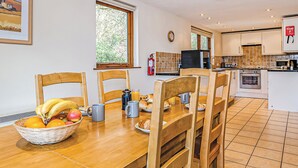A dining area with a wooden table, chairs, a fruit basket, and a kitchen in the background. - Luxury lodge residing at the top of the wooded valley. (Waterrow, Wiveliscombe)