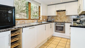 A modern kitchen with white cabinets, a built-in oven, a microwave, and a window with a view of trees. - Luxury lodge residing at the top of the wooded valley. (Waterrow, Wiveliscombe)